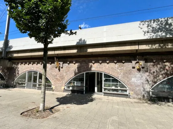 Bakstenen spoorviaduct met boogvormige ramen en deuren van bedrijven, waaronder 'Tussen de Bogen'.